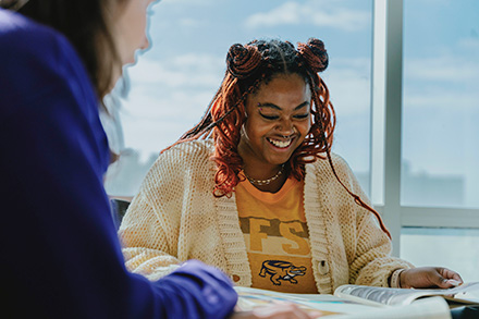 An SFSU student smiles while looking down at a book in the light-filled library.