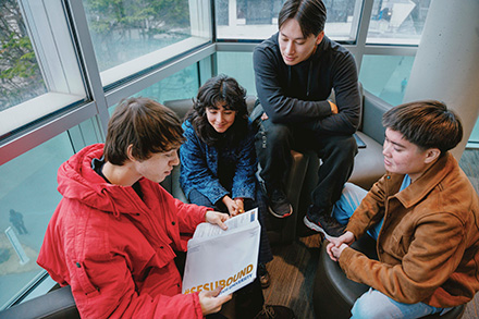 A student opens their SFSU offer of acceptance while three other students look on excitedly.
