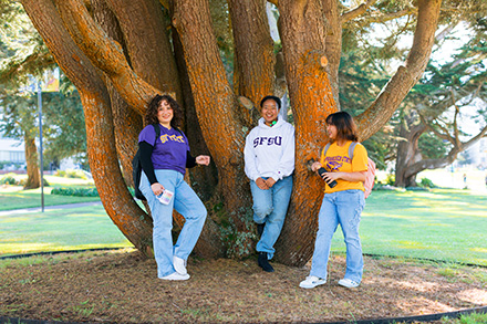 Three SFSU students laugh together under a tree on campus.